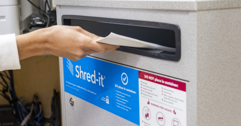 Secure Shred-It bin showing a hand inserting documents into it.