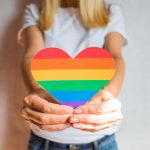 Woman holds in hands a heart in the colors of the rainbow. Young beautiful girl. LGBT history month. Pride Month. Lesbian Gay Bisexual Transgender. LGBT flag. Love, human rights, tolerance. LGBTQ+