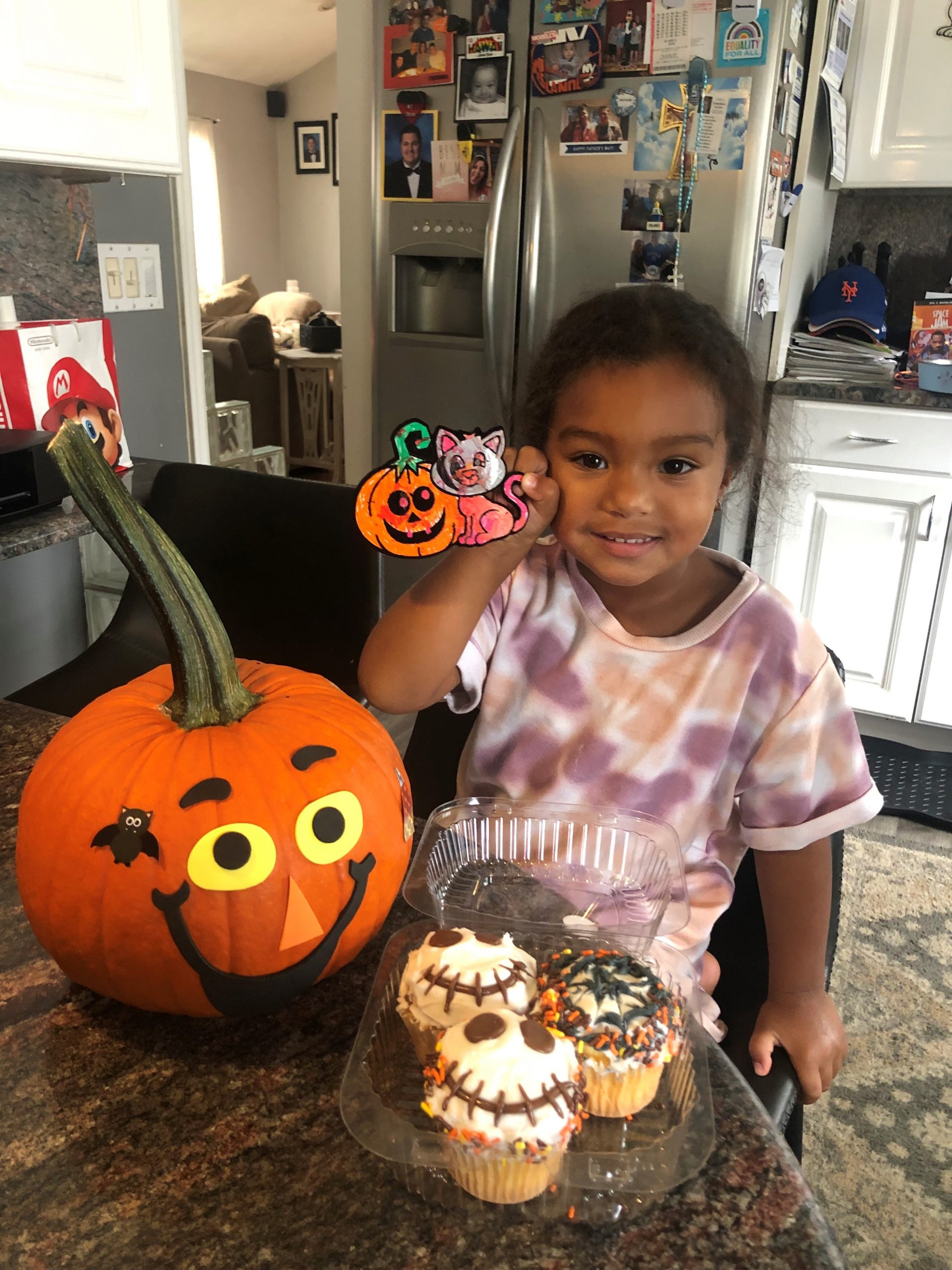 a child holding a diy craft and a decorated pumpkin and cupcakes on a table