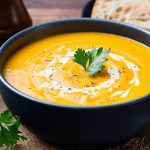 Pumpkin and carrot soup with cream and parsley on dark wooden background.