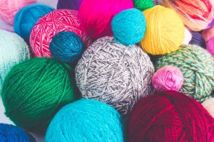 About 15 balls of yarn in various colors like yellow, aqua, burgundy, pink, green, etc.