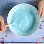 a little girl hands making slime herself on blue wooden background