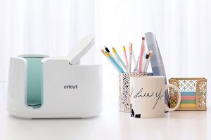 Cricut mug press machine with two different mugs with designs on them next to it sitting on a desktop.