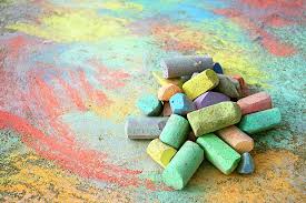 Pieces of chalk in various colors like green, yellow, purple, and pink sitting in a pile on top of a sidewalk that has been colored.