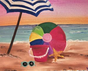 A beach umbrella, beach ball, pail, starfish, and sunglasses sitting on the beach with the ocean in the background.