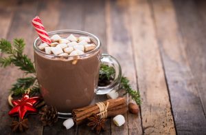 A mug of hot chocolate with marshmallows and a candy cane on a wooden table.