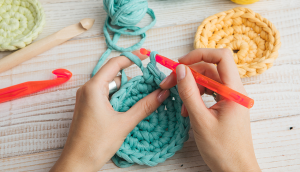 A set of hands crocheting a circle in a teal-colored yarn.