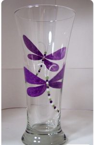 A clear glass vase with purple dragonflies painted on it.