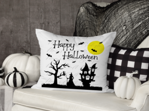 A decorative pillow with Happy Halloween with a spooky house, witch, and a tree.