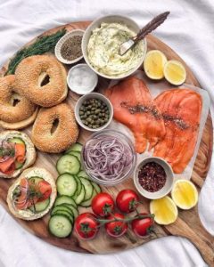 Bagel breakfast board with lox, bagels, cream cheese, cucumbers, tomatoes, onions, and hard boiled eggs.