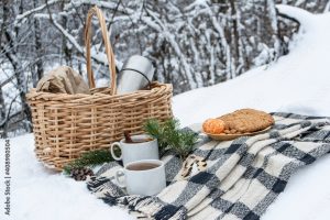 A picnic basket, blanket, and various foods set out on a snowy bank.