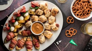 A platter of game day appetizers with meatballs, pigs in a blanket, and pretzels.