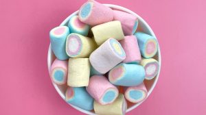 Colored marshmallows in a white bowl on a pink background