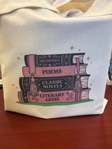 A tote bag with a stack of 4 books with Memoirs, Poems, Classic Novels, and Literary Gems written on the spine.