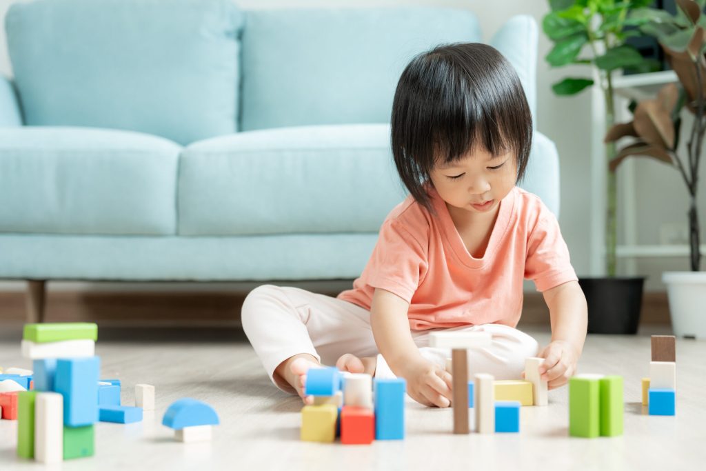 A little girl playing with different types of blocks on the living room floor.