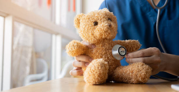 A person in scrubs holding a stethoscope to a teddy bear's chest.